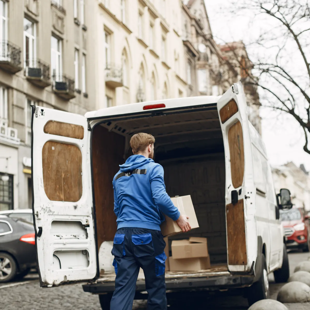 Agencia de transportes en Madrid: operario cargando una caja en una furgoneta blanca con las puertas traseras abiertas